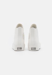 Zapatillas altas blancas con material suave, suela de goma, parche de logo en la parte trasera y diseño minimalista sin patrones visibles.