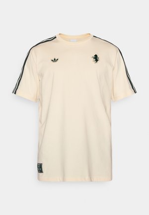 Cremefarvet bomulds T-shirt med sorte sidestriber, med en grøn broderet løve og et logo på brystet. Korte ærmer, lige kant.