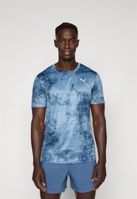 Blauwe sport T-shirt met een gestructureerd, abstract ontwerp en een witte logo op de linkerborst. Korte mouwen en een ronde hals.