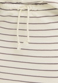 Gros plan sur un tissu crème avec de fines rayures horizontales grises et un cordon blanc noué au centre.