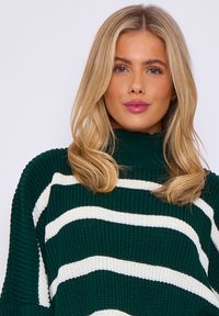 Chunky green knit sweater with white horizontal stripes; features a high neck and relaxed fit, showcasing textured fabric and stitch pattern.