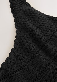 Sort hæklet stof med strukturerede mønstre, der har hævede masker og bølgede kanter, der fremhæver en blød, vævet struktur.