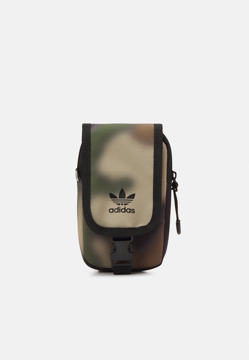 Bolsa de tela de camuflaje con ribete y correa negra. Presenta una solapa plegable, cierre a presión y el logo de Adidas en negro.