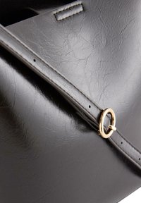 Svart faux läderhandväska med en slät textur, med en detalj i guldmetallringsform och en strukturerad, vinklad design.