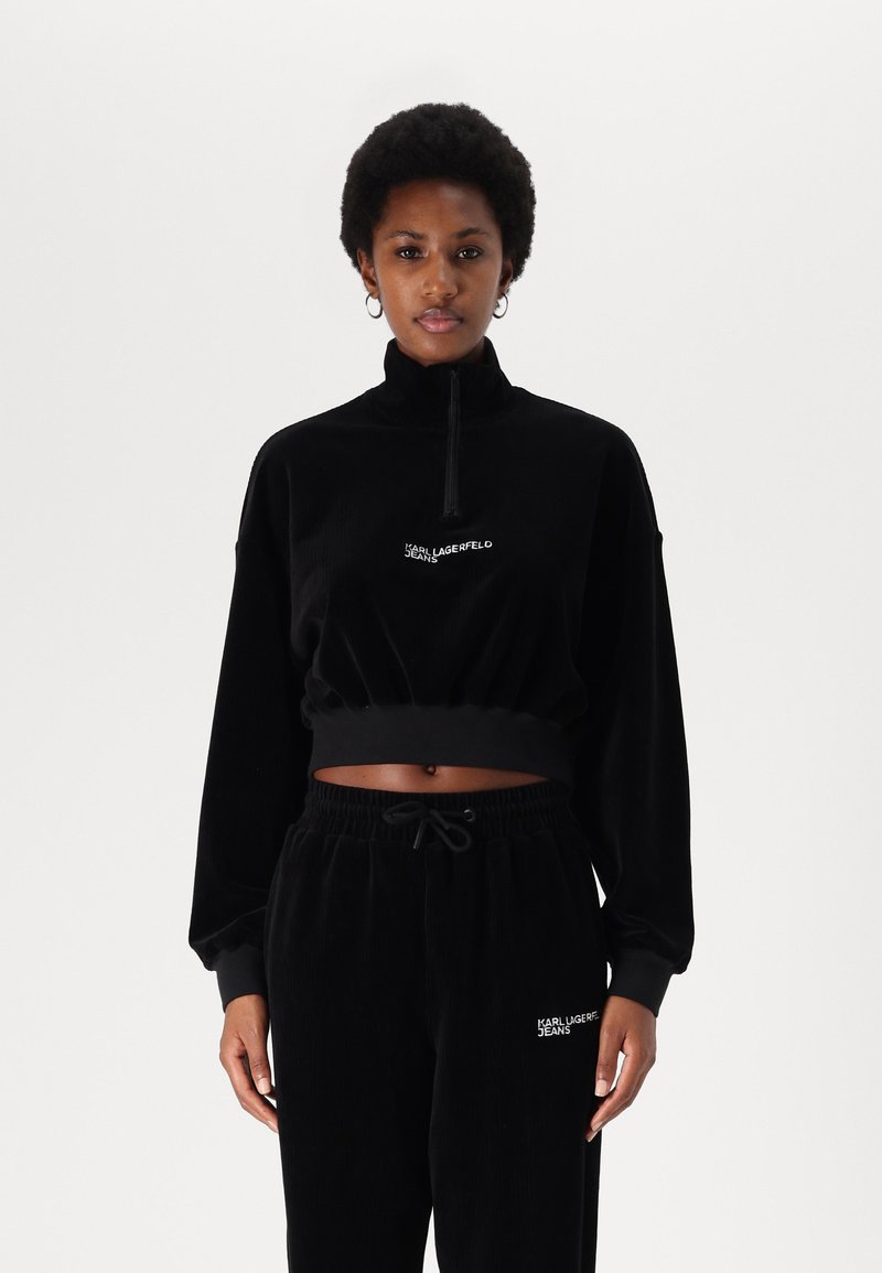 Black corduroy zip-up sweatshirt with a cropped design; features long sleeves, a high collar, and embroidered logo. Paired with matching pants.