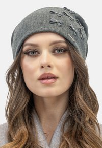 Cappello grigio in feltro con un design morbido, impreziosito da multiple spille decorative grigie scure e perle finte. Texture liscia.