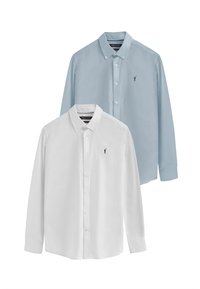 Två skjortor med knappar: en vit och en ljusblå, båda med lång ärm och små broderade logotyper på vänster bröst.