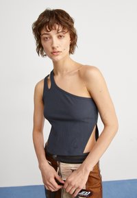 Top a maniche corte asimmetrico grigio scuro a costine con una fessura laterale e dettaglio del logo all'orlo, abbinato a pantaloni marroni con grafica.