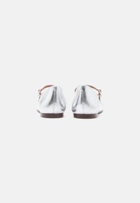 Ασημένια μεταλλικά φλατ παπούτσια με απαλό υλικό, στρογγυλεμένη μύτη και αντίθετη σκουρόχρωμη καφέ σόλα. Διαθέτουν ένα μικρό φιόγκο στη πλευρά.