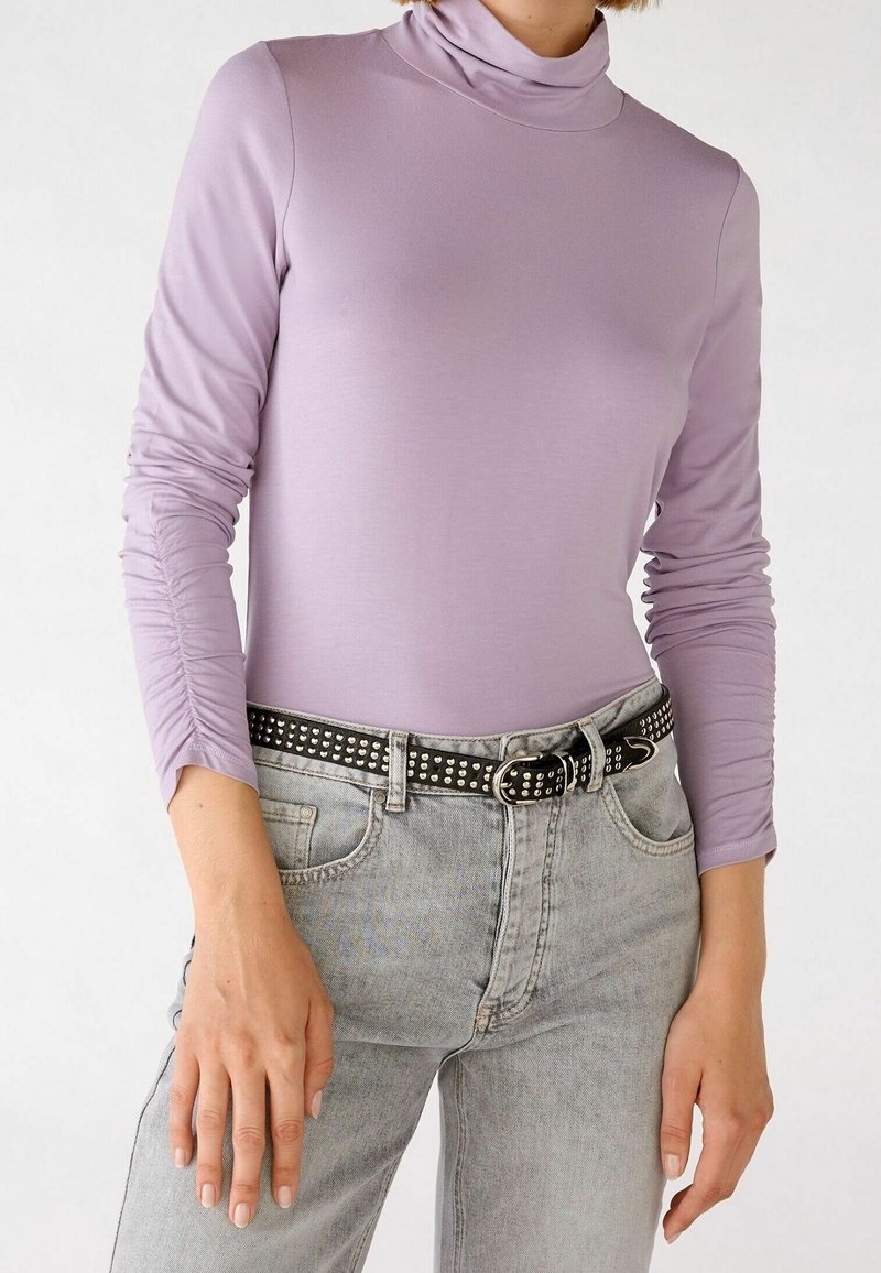Personne portant un pull-over léger violet à manches longues avec des manches froncées et un jean gris clair avec une ceinture cloutée noire.