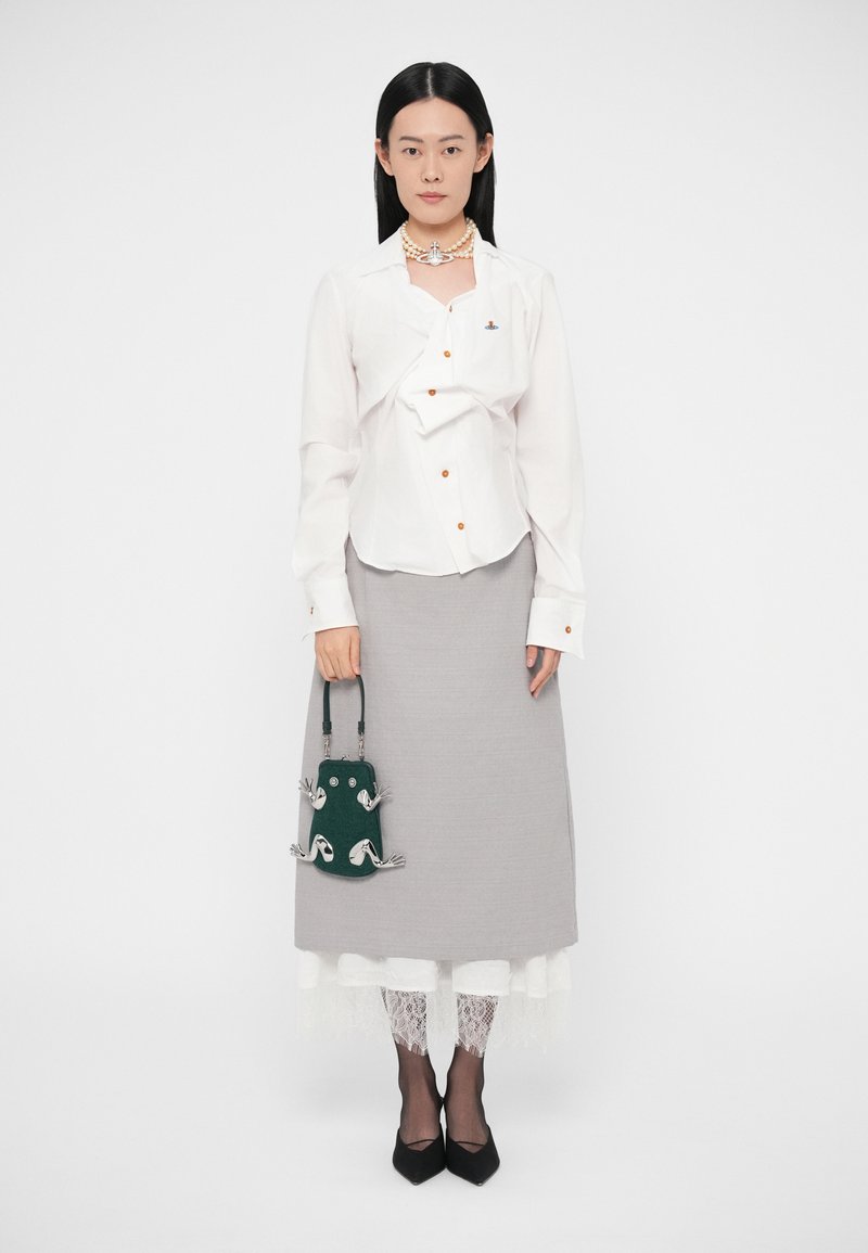 Witte blouse met knopen en oranje accenten, grijze rok tot op de knie, groene handtas met textuur en zwarte puntige schoenen. Details met kantafwerking zichtbaar.