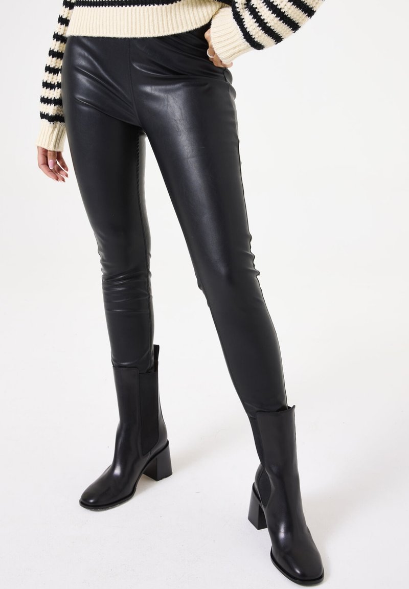 Zwarte faux leren leggings met een strakke, getailleerde pasvorm. Gecombineerd met zwarte enkellaarsjes met hak en elastische zijpanelen.