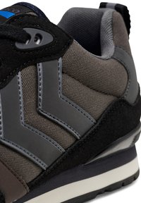 Gray sneaker with textured fabric, suede accents, and plastic eyelets. Features zigzag gray stripes on the side and a white sole.