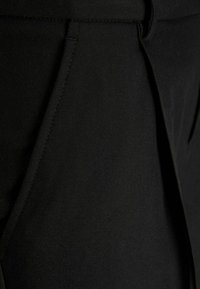 Zwarte broek met een gladde stoftextuur, gestructureerd ontwerp, scherpe vouw en subtiele details op de tailleband en zakken.