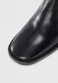 Stivale alla caviglia in pelle nera con superficie liscia, punta rotonda e design minimalista. Presenta una suola in gomma nera piatta.