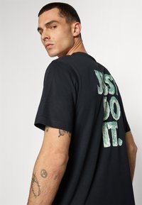Sort bomulds t-shirt med korte ærmer, rund hals og et stort slidt tekstgrafik på ryggen der står "JUST DO IT."
