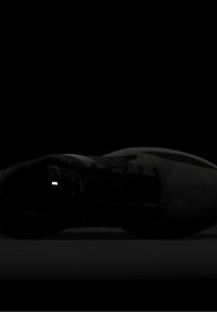 Chaussure de sport gris foncé avec des lacets noirs, couchée sur le côté sur un fond noir.