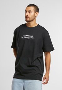 Sort bomulds t-shirt med korte ærmer og rund hals, med hvid tekst der står "Las Vegas The Gambling Capital" på forsiden.