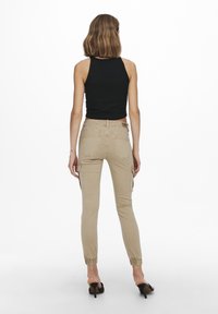 Beige cargobroek met opgerolde enkels, meerdere zijzakken en een slim fit ontwerp, gecombineerd met een zwarte mouwloze geribbelde top.