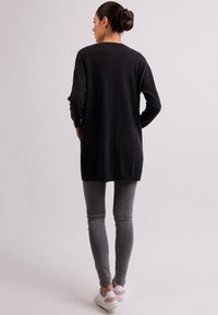 Maglione nero a maniche lunghe con vestibilità comoda, texture morbida e scollo rotondo, abbinato a jeans skinny grigi chiari e sneaker bianche.