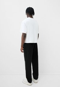 Bílý krátký rukáv tričko, volný střih, v kombinaci s černými volnějšími džíny a bílými teniskami. Minimalistický design, žádné viditelné logo nebo vzory.