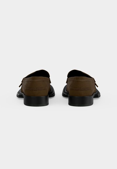 Ζεύγος καφέ δερμάτινων loafers με μαύρες φτέρνες, που φαίνονται από πίσω σε απλό ανοιχτό γκρι φόντο.