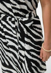 Abito a righe zebrate in bianco e nero, con dettaglio della vita annodata. Realizzato in un tessuto liscio con una consistenza morbida e fluida.