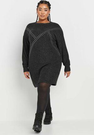 Schwarzes Strickkleid mit langen Ärmeln, das ein dekoratives Muster aus silbernen Nieten an den Schultern und der Brust aufweist, sowie eine entspannte Passform hat.