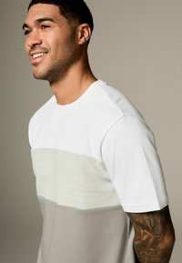 T-shirt à manches courtes avec une partie supérieure blanche, un milieu à rayures gris clair et une partie inférieure grise unie. Fabriqué en coton doux.