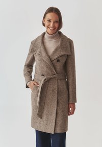 Bruine textuur wol coat met grote kraag, dubbele knopen, ceintuur in de taille en zijzakken. Draag dit over een lichte turtleneck.
