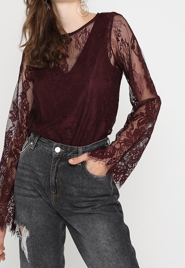 Bordeaux blonde top med lange gennemsigtige ærmer, der har blomster mønstre og en V-halsudskæring, parret med højtaljede mørke jeans.