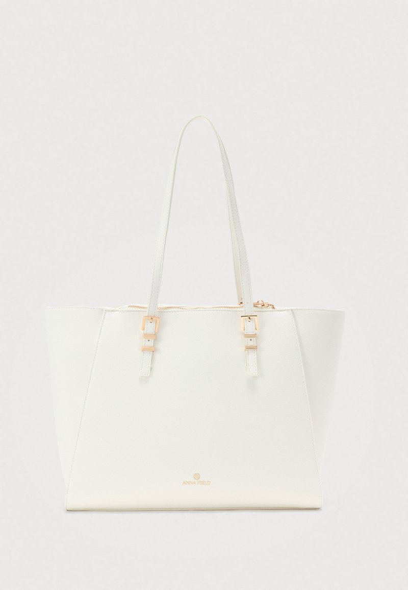 Sac fourre-tout rectangulaire blanc avec double anses plates, boucles dorées, fermeture éclair et petit logo doré "Anna Field" sur le devant.