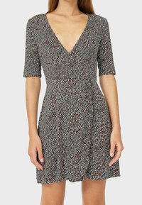 Vestido de patrón blanco y negro con escote en V, mangas cortas y falda acampanada, que presenta acentos rojos y un corsé ajustado.