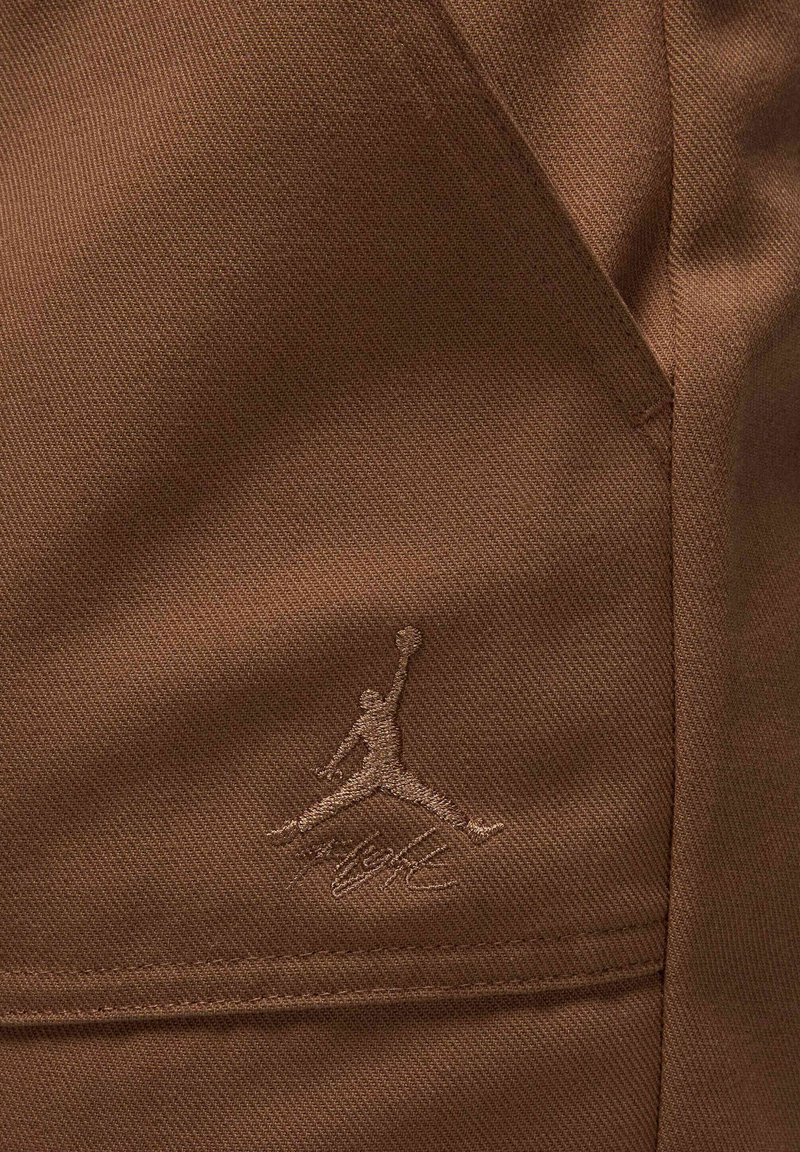 Un tessuto marrone presenta il logo Air Jordan ricamato in una tonalità leggermente più chiara. La texture è liscia con un motivo di intreccio resistente.