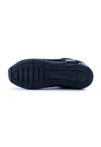 Suela de zapatilla negra con goma texturizada, que presenta un patrón estriado para agarre. Incluye un parche con el logo en el costado. Forma plana y ancha.