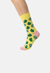 Gele sokken met groene limoen en ronde limoen plakjes patronen, roze hiel en teen accenten, gemaakt van een zacht textielmateriaal.