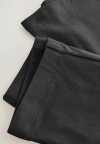 Schwarze Baumwollleggings mit glatter Textur, gefaltet mit sauberen Nähten entlang der Kanten, bieten ein schlichtes, funktionales Design.