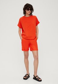 Felrood bijpassend set bestaande uit een top met korte mouwen met bladeren borduursel en short met zakken. Inclusief zwarte sandalen met bandjes.