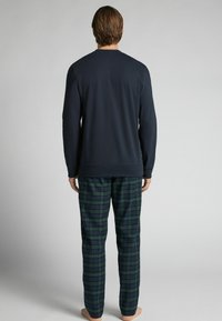 Námořnická mikina s dlouhými rukávy v kombinaci se zeleno-modrými kostkovanými pyžamovými kalhotami. Směs bavlny, volný střih a elastický pás.