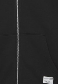 Zwarte rits-hoodie van premium stof, voorzien van een zilveren rits, voorzakken en een klein label in de rechteronderhoek.