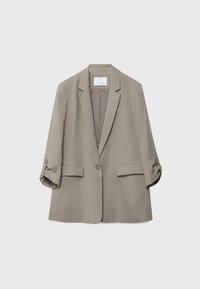 Blazer marron clair à un bouton avec revers crantés, manches retroussées et deux poches à rabat à l'avant sur fond uni.