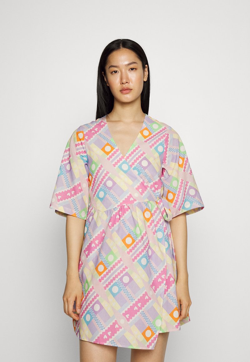 Vestido de manga curta em tecido leve, com um padrão geométrico colorido de círculos e ziguezagues sobre um fundo pastel.