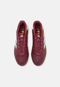 Zapatillas deportivas burdeos con parte superior texturizada, franjas blancas de acento y un cuello acolchado. Presenta un diseño de cordones y una suela de goma.