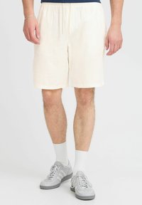 Cream-colored linen shorts with an elastic waistband, falling to mid-thigh, paired with gray sneakers and white socks.