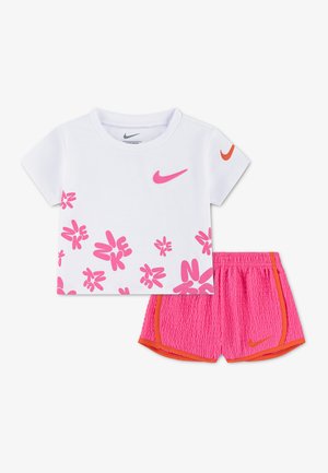 Balta Nike trumpomis rankovėmis marškinėliai su rožiniais gėlių raštais ir rožinės spalvos šortai su oranžiniu apvadu ir Nike logotipais ant balto fono.