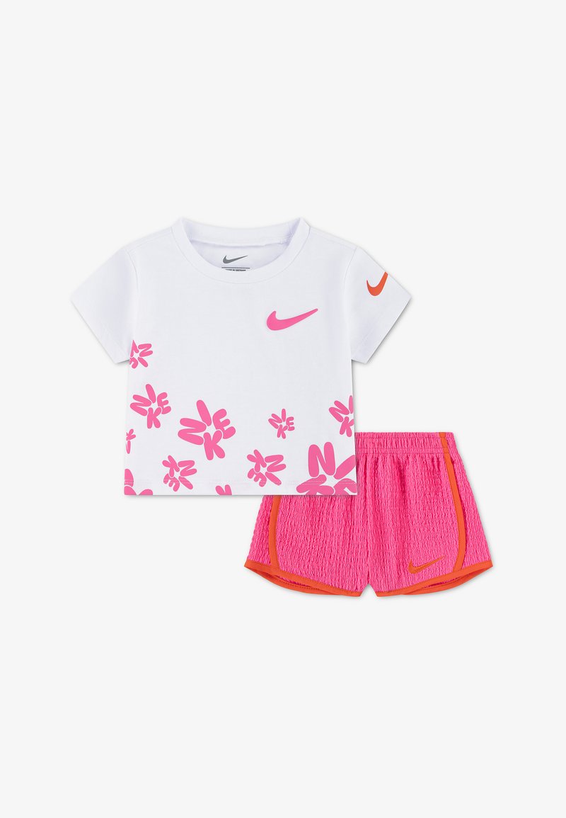 Λευκό κοντομάνικο μπλουζάκι Nike με ροζ υφασμάτινα σχέδια λουλουδιών και ροζ σορτς με πορτοκαλί περιθώριο και λογότυπα Nike σε λευκό φόντο.