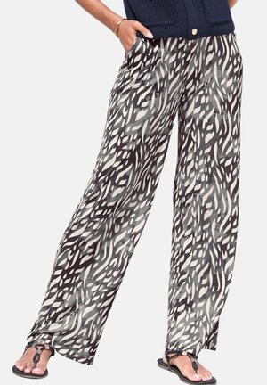 Wide-leg pants with black and white abstract animal print, worn with black sandals and a dark textured top, hands in pockets.