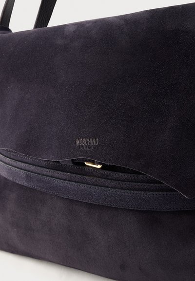 Sac à main Moschino Milano en daim noir avec fermeture à rabat et détail discret de boucle dorée.