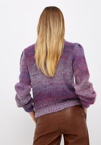 Gestrickter Pullover in Violett- und Pinktönen mit strukturierter Oberfläche. Verfügt über gepolsterte Ärmel und einen gerippten Saum. Kombiniert mit braunen Lederhosen.