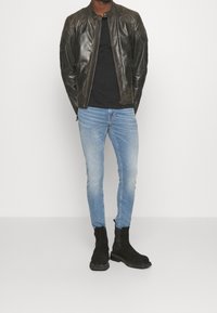 Svart läderbomberjacka, åtsittande svart t-shirt, ljusblå slim-fit jeans och svarta ankelstövlar. Har en slät textur och minimalistisk design.